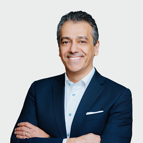 Professional head-and-shoulders portrait of a smiling man in a navy suit with a white shirt and pocket square, neutral light background.