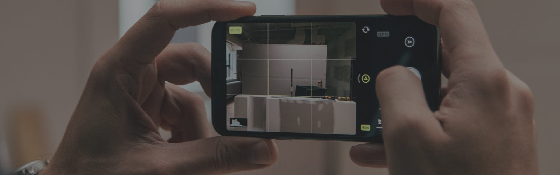 Person holding a smartphone and filming a room with stacked boxes visible on the screen; grid overlay on the display.