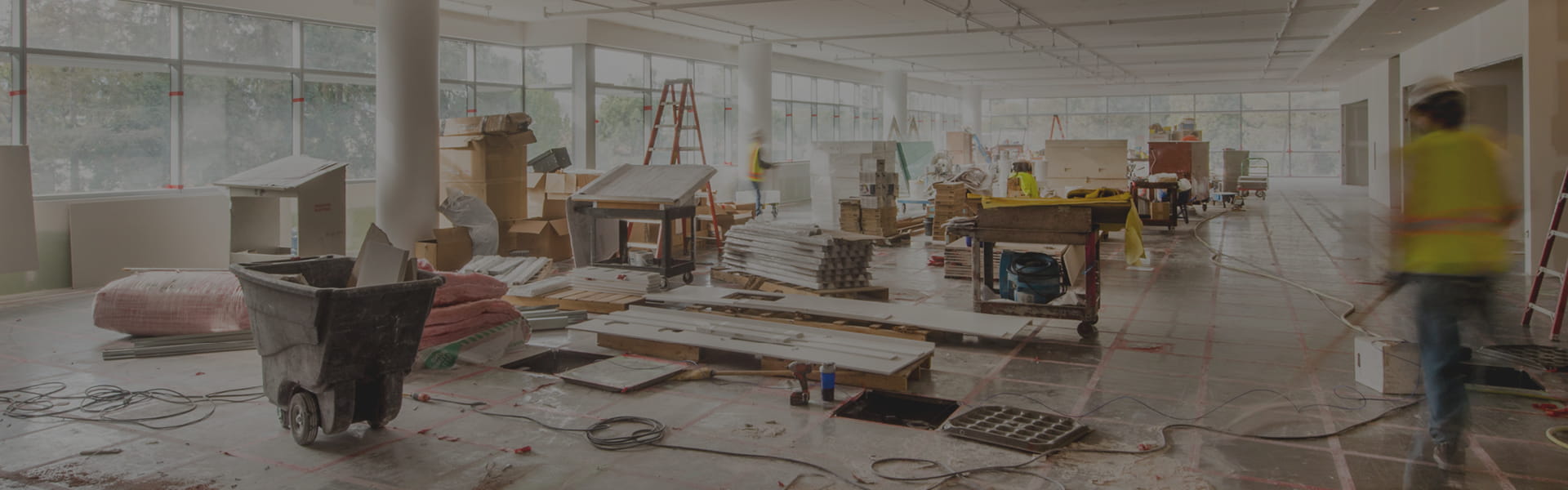 Open-concept interior under renovation with workers, ladders, and scattered construction materials across the floor.