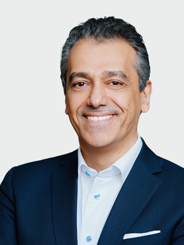 Portrait of a smiling man in a navy suit and white shirt against a light neutral background.