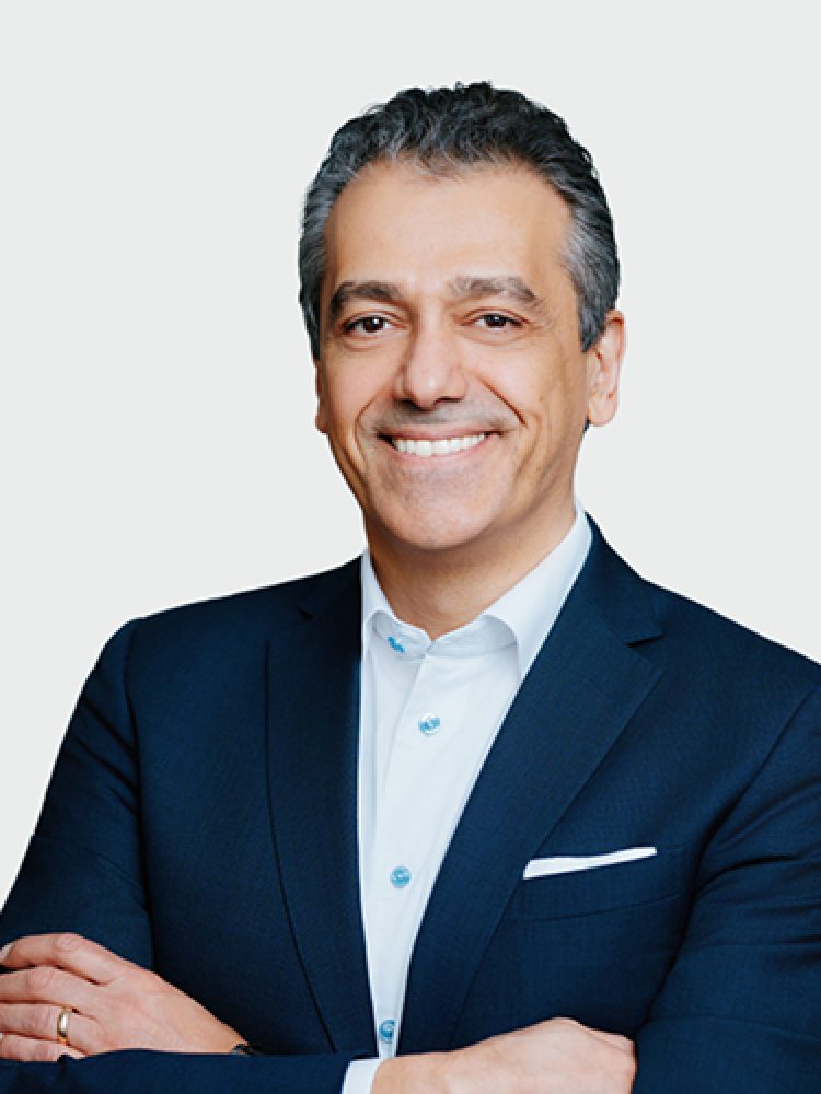 Professional head-and-shoulders portrait of a smiling man in a navy suit with a white shirt and pocket square, neutral light background.